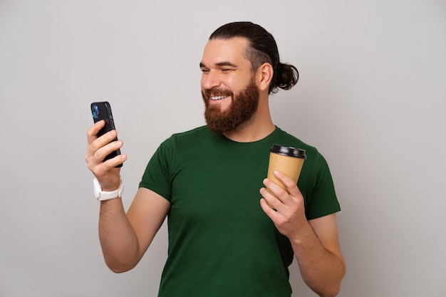 Homem sorridente lê notícias nas redes sociais enquanto segura o telefone e vai tomar café