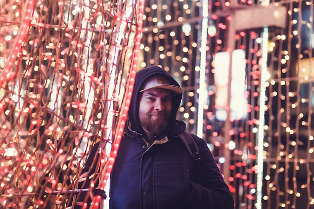 Foto homem sorridente legal em um boné no fundo da iluminação da cidade à noite