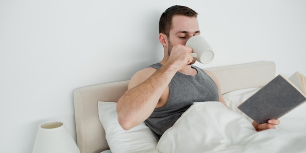 Homem sorridente lendo um romance enquanto toma um chá