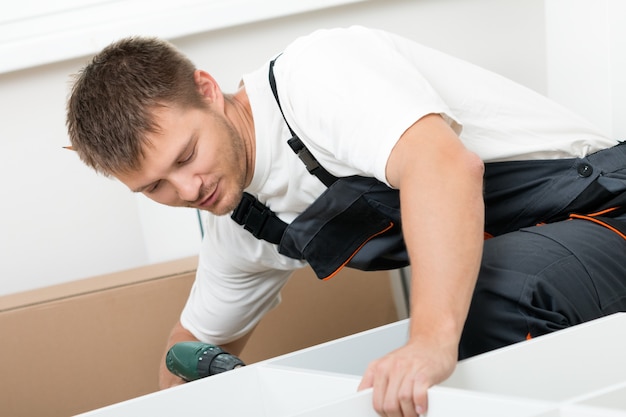 Homem sorridente montando móveis de auto-montagem na nova casa. DIY, nova casa e conceito de mudança