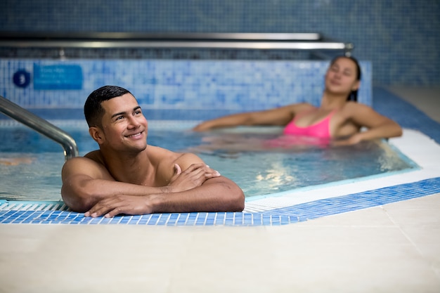 Homem sorridente na piscina com a namorada