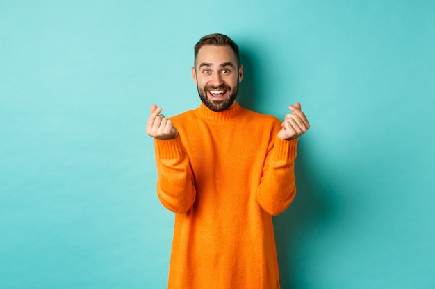 Homem sorridente, parecendo feliz, gesto de sorte, vestindo um suéter laranja