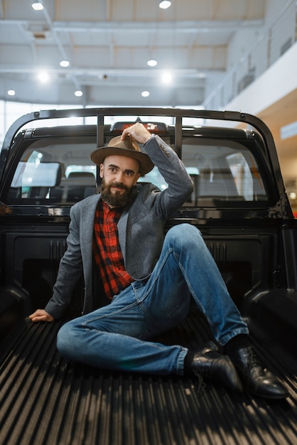 Homem sorridente posa na parte de trás da nova caminhonete na concessionária. cliente no showroom de veículos, homem comprando transporte, concessionária de automóveis