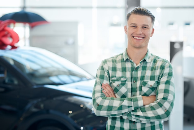 Homem sorridente posando perto de carro.