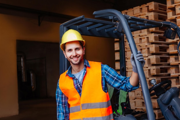 Homem sorridente posando perto de empilhadeira industrial no armazém