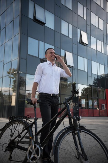 Homem sorridente respondendo ao telefone inteligente enquanto está de pé com uma bicicleta na cidade