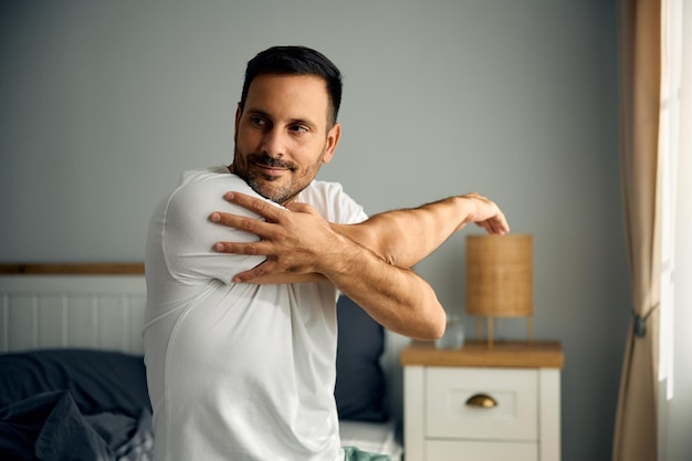 Homem sorridente se alongando enquanto acorda no quarto pela manhã