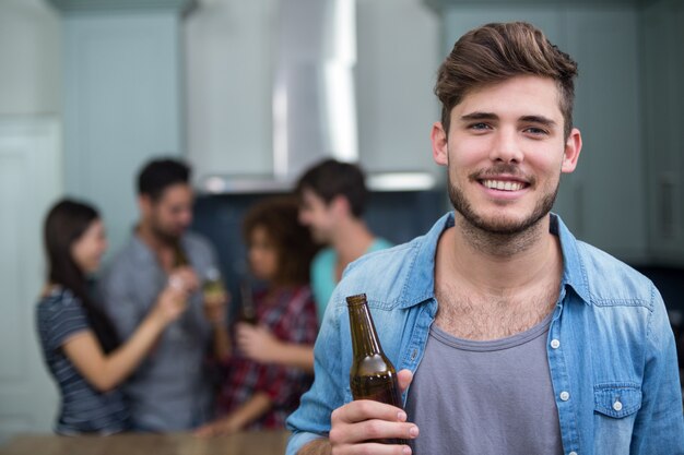 Homem sorridente segurando a garrafa de cerveja enquanto amigos