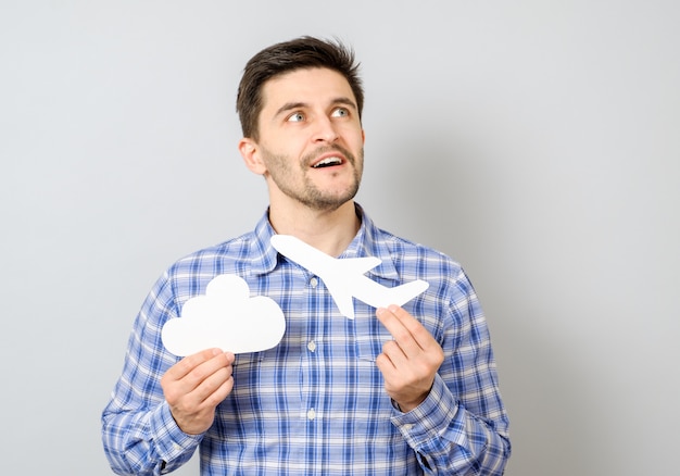 Homem sorridente segurando modelo de papel branco de avião e nuvem