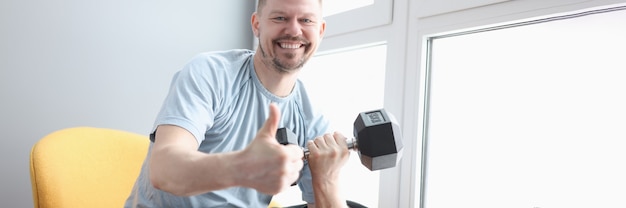 Homem sorridente segurando um haltere e mostrando o gesto de polegar para cima