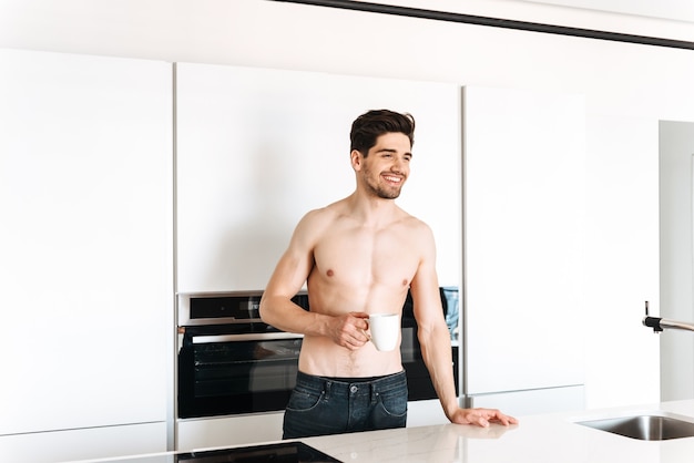 Homem sorridente sem camisa bebendo café em pé