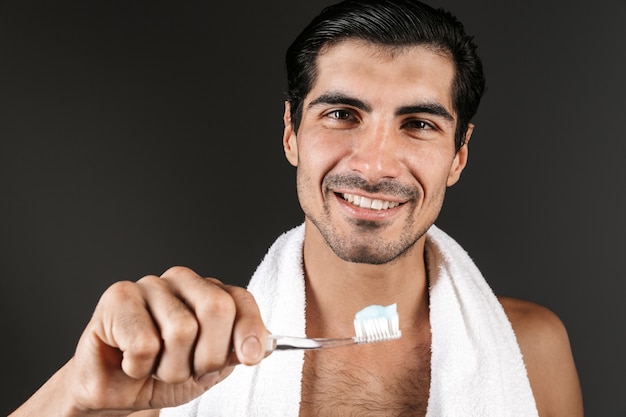 Homem sorridente sem camisa com uma toalha nos ombros, isolado, segurando uma escova de dentes