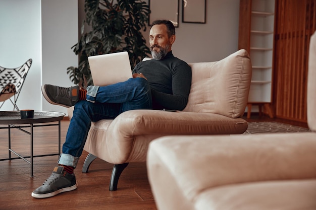 Homem sorridente sentado na poltrona e usando laptop