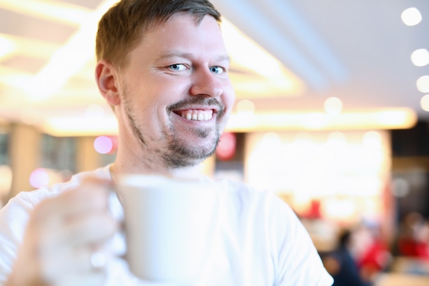 Homem sorridente, sentado no café com uma xícara grande de café