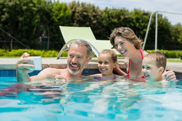 Homem sorridente tirando uma selfie com a família na piscina