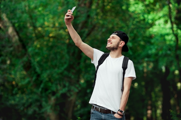 Homem sorridente tirando uma selfie contra árvores verdes em um parque público