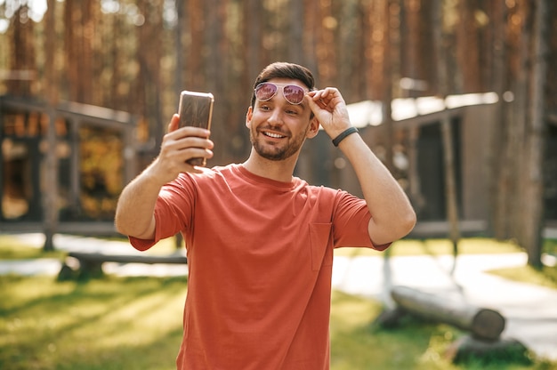 Homem sorridente tocando óculos tirando uma selfie