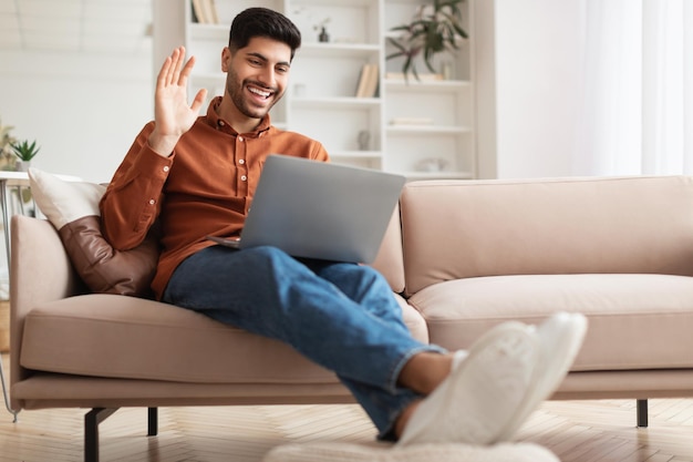 Homem sorridente trabalhando no laptop acenando com a mão