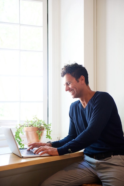 Homem sorridente, usando computador portátil, casa
