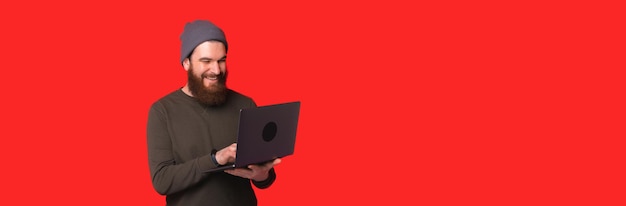 Homem sorridente usando laptop perto de fundo vermelho
