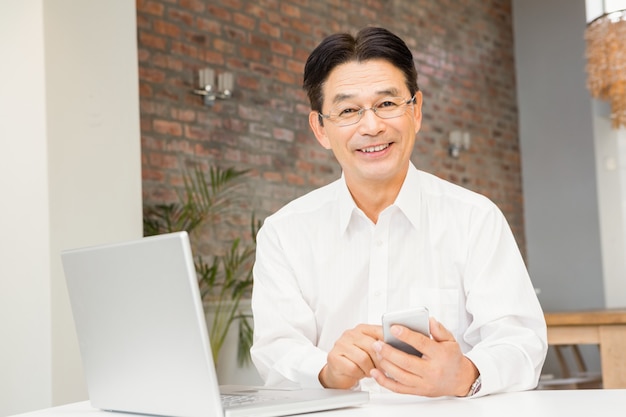 Homem sorridente, usando, smartphone, e, laptop, em, sala de estar