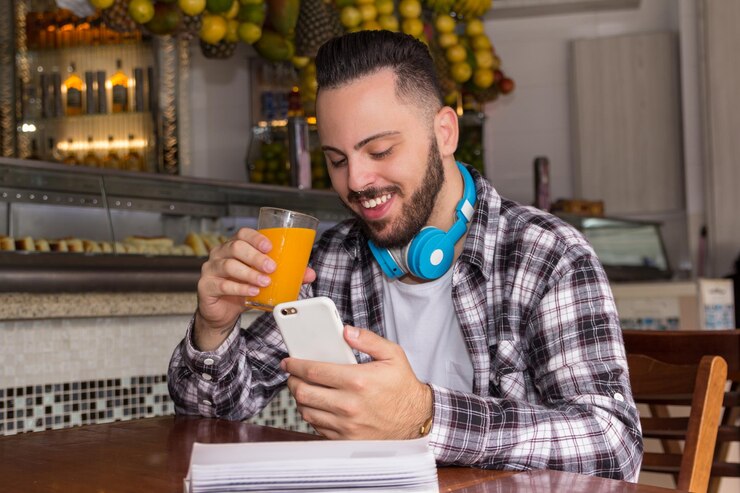 Foto homem sorridente usando telefone celular enquanto bebe suco em um restaurante
