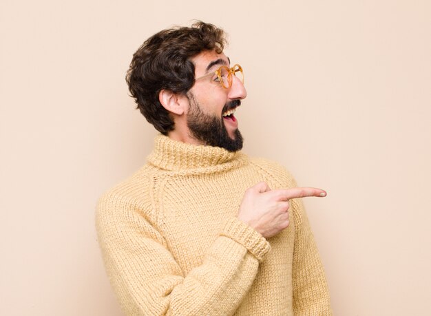 Homem sorrindo alegremente, sentindo-se feliz e apontando para o lado e para cima, mostrando o objeto no espaço da cópia