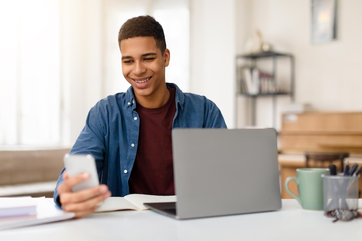 Foto homem sorrindo ao telefone com laptop na mesa