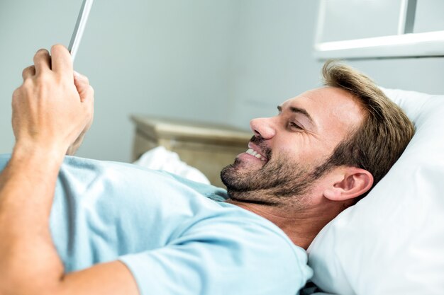 Homem sorrindo enquanto estiver usando o celular na cama em casa