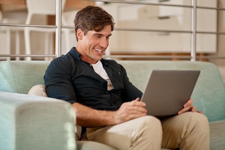 Foto homem sorriso e laptop em casa no sofá feliz e e-mail para comunicação mídias sociais e computador apartamento online e tecnologia para trabalho remoto freelancer ou reunião virtual com pc e streaming