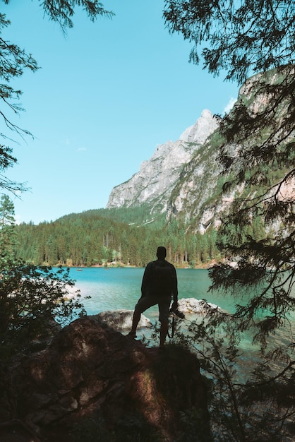 Homem subindo por rochas para fotografar bela paisagem de lago e montanhas