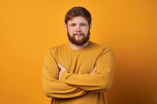 Homem sueco atraente com barba e cabelo elegante, ri de uma história engraçada de um amigo com as mãos cruzadas e os olhos fechados.