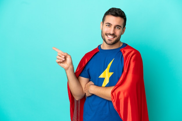 Homem super-herói caucasiano isolado em fundo azul apontando o dedo para o lado