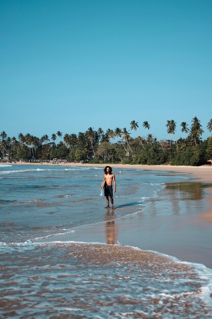 Homem surfista sentado na prancha de surfe na areia da praia