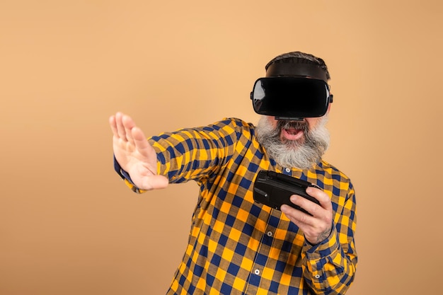 Homem surpreso em posar de camisa casual isolado em um fundo amarelo no estúdio. Conceito de estilo de vida de pessoas. Assistindo com óculos de realidade virtual, brincando com joystick