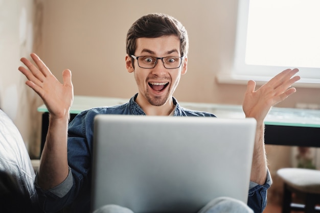 Homem surpreso feliz com laptop em casa, recebi e-mail agradável, boas notícias, ganhei na loteria