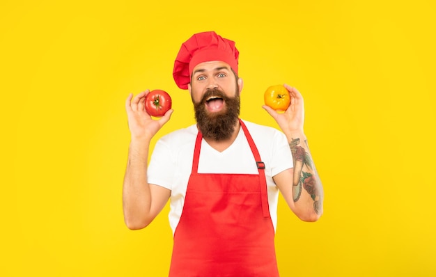 Homem surpreso no avental de cozinha e toque segurando o chef de fundo amarelo de tomate