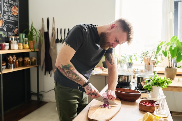 Homem tatuado cortando cebola na cozinha