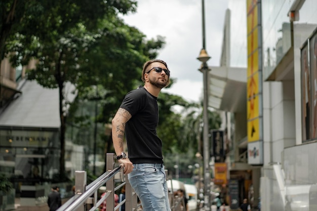 Homem tatuado feliz atraente sorrindo na rua em Kuala Lumpur. Homens urbanos, estilo de roupa. Bolhas de sabão voam no ar.