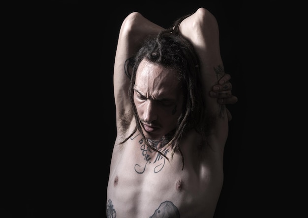 Homem tatuado. O retrato do hipster parece brutal. Corpo de moda masculina. Homem bonito e elegante, pose em um fundo escuro. Aparência forte e brutal. Retrato de um cara moderno com dreadlocks.