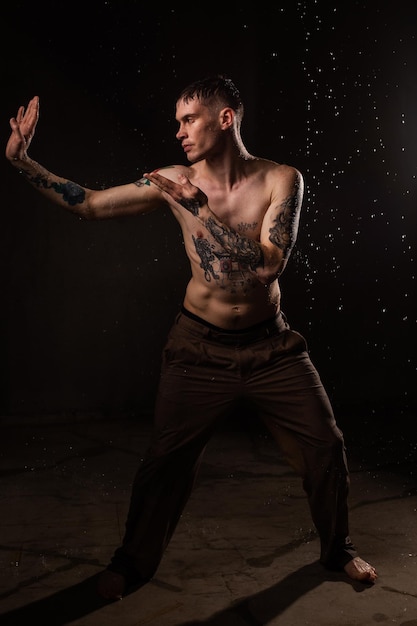 Homem tatuado sexy e saudável com gotas de água em seu corpo Retrato de estúdio masculino de moda de torso nu