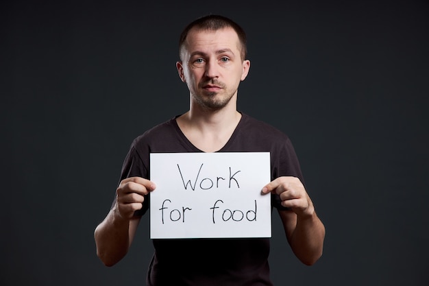 Homem tem nas mãos uma folha de papel de pôster com a inscrição Eu trabalho por comida.