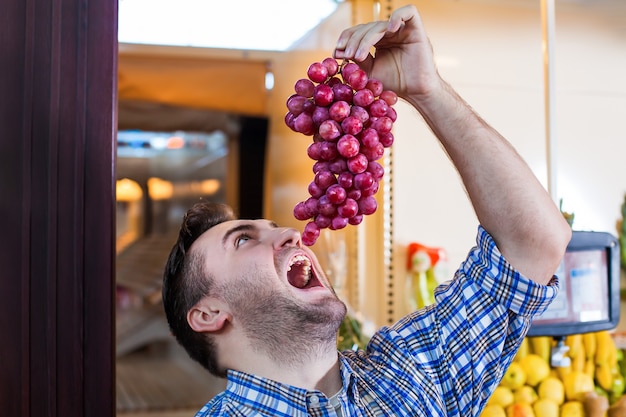 Foto homem tentando comer um cacho de uvas.