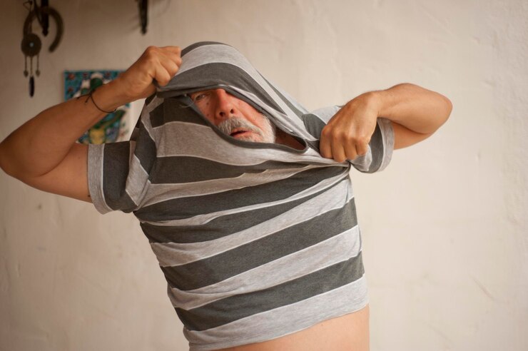 Foto homem tirando a camiseta enquanto está de pé contra a parede em casa