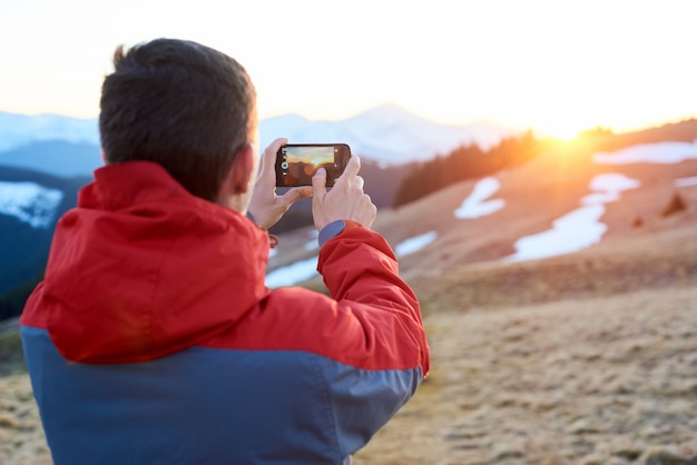 Homem tirando foto da maravilhosa paisagem nas montanhas durante o pôr do sol colorido da primavera