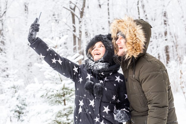 Homem tirando foto de selfie jovem casal romântico sorrir neve floresta inverno ao ar livre.