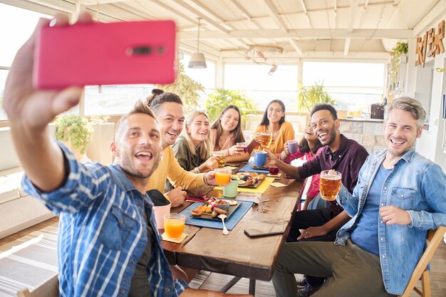 Foto homem tirando selfie de celular com um grupo multirracial de amigos em um bar