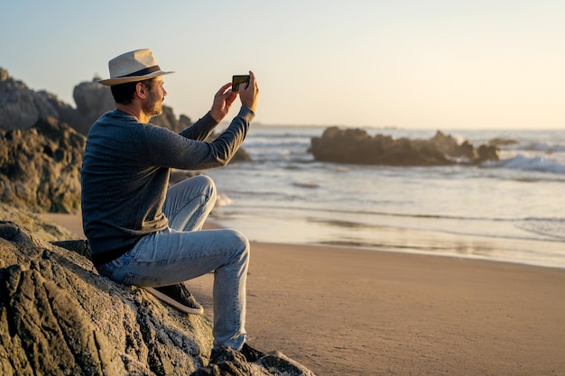 Homem tirando selfies com smartphone e sorrindo na praia happyx9