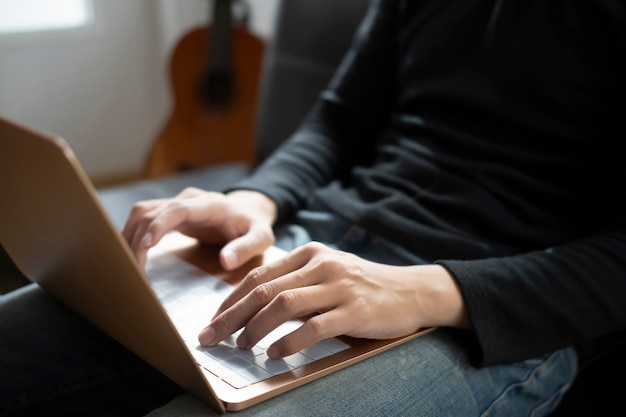 Homem tiro recortado usando o computador laptop enquanto está sentado no sofá em casa.