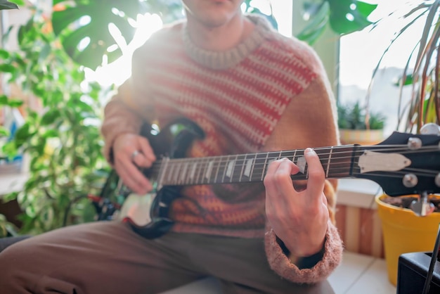 Homem tocando guitarra elétrica em seu lugar favorito entre plantas verdes em casa. Zona de conforto pessoal